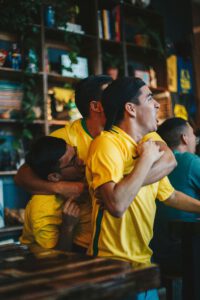 A group of joyful soccer fans in yellow jerseys celebrating a goal in a pub.